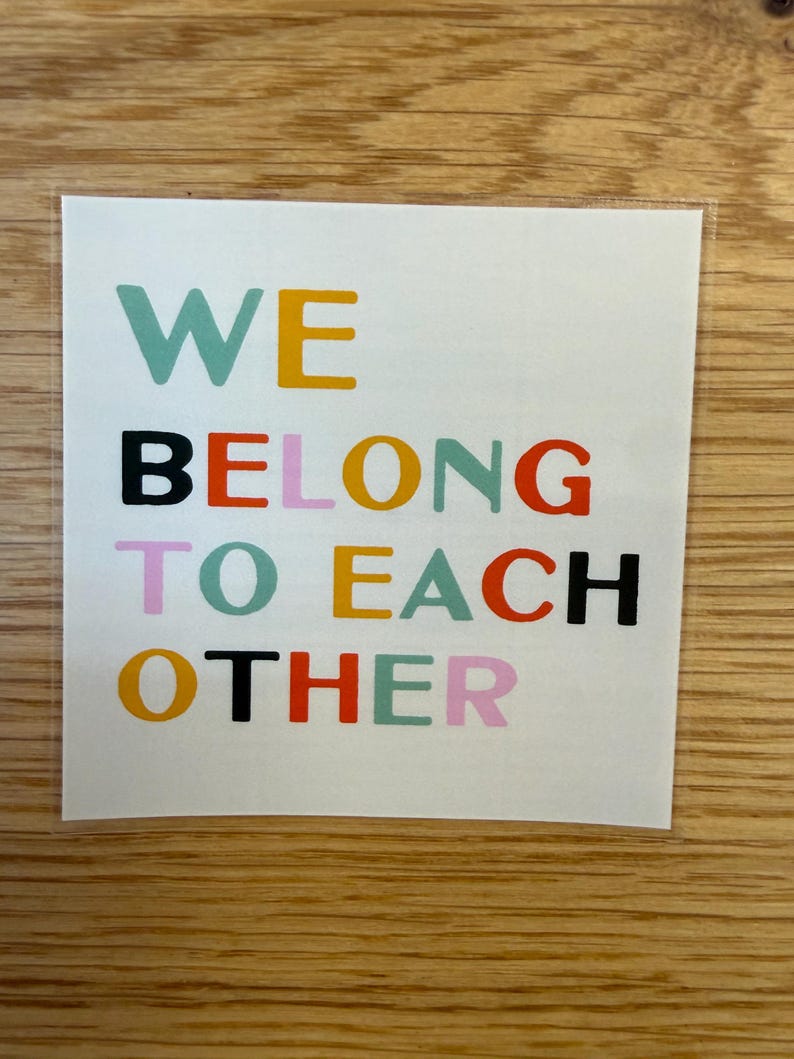 May include: A square sticker with the words "WE BELONG TO EACH OTHER" in various colors. The text is arranged in three lines, with each word in a different color, including teal, yellow, black, orange, pink, and red.