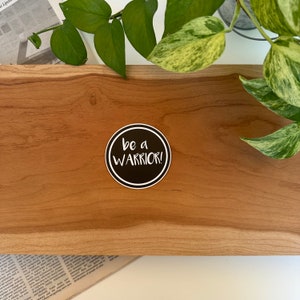 May include: A black and white round sticker with the text "be a WARRIOR!" in white lettering on a black background.