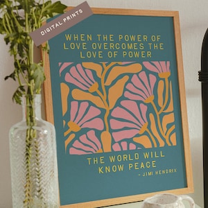 Op de afbeelding: Een ingelijste kunstdruk met een teal achtergrond en een bloemenontwerp in roze en oranje. De print bevat de quote "When the power of love overcomes the love of power, the world will know peace" van Jimi Hendrix. De lijst is van licht hout.