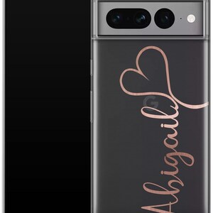 May include: A clear phone case with a black background and a rose gold heart design and the name "Abigail" in cursive script. The phone case is on a black smartphone.