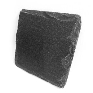 Puede incluir: Una tabla de servir de pizarra negra con una superficie rugosa y texturizada. La tabla es rectangular y tiene bordes ligeramente irregulares.
