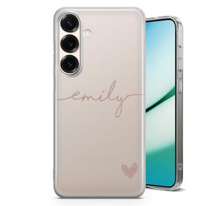 May include: A clear phone case with a pinkish-beige background. The name "emily" is written in a cursive, glittery pink font. A small glittery pink heart is below the name. The phone case is on a smartphone.