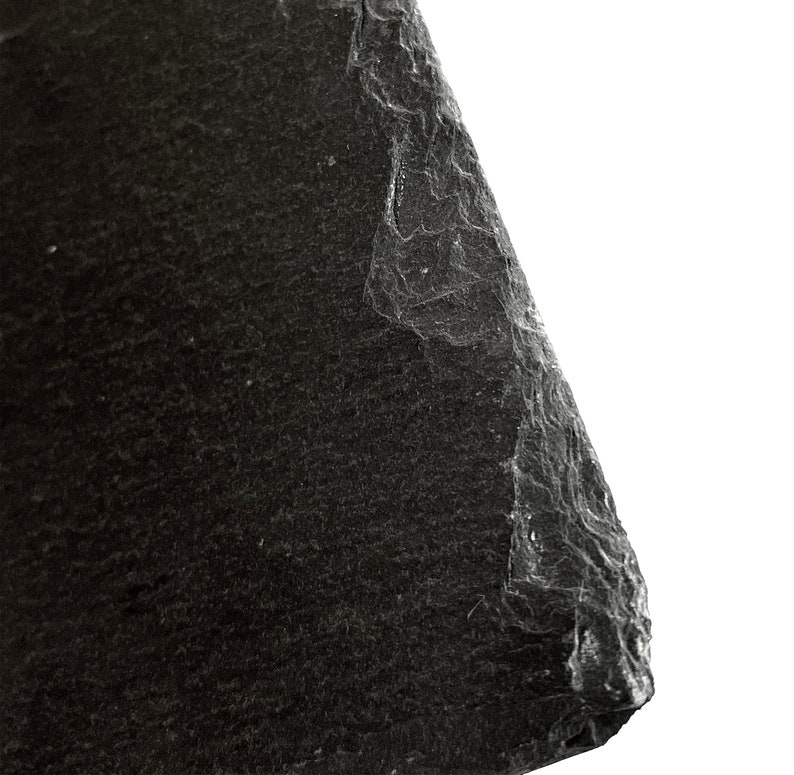 Puede incluir: Primer plano de una roca de pizarra gris oscuro con una superficie rugosa y texturizada. La roca tiene un borde irregular y est&aacute; inclinada hacia el lado derecho de la imagen.