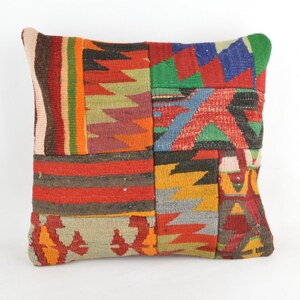 Puede incluir: Cojín decorativo cuadrado con diseño de patchwork. El cojín presenta una variedad de colores, incluyendo rojo, naranja, verde, azul y amarillo. El diseño de patchwork está compuesto por formas y patrones geométricos.
