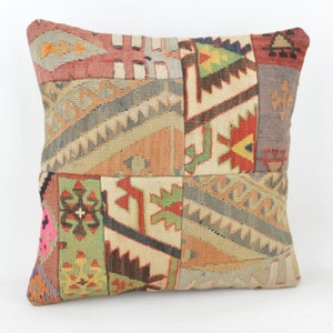 Puede incluir: Cojín decorativo cuadrado con diseño de patchwork. El cojín presenta una variedad de colores, incluyendo rojo, verde, beige y gris. El cojín tiene un aspecto texturizado y probablemente está hecho de tela tejida.