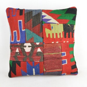 Puede incluir: Cojín decorativo cuadrado con diseño de patchwork. El cojín presenta una variedad de patrones geométricos en rojo, azul, verde y negro. El cojín está hecho de tela tejida.