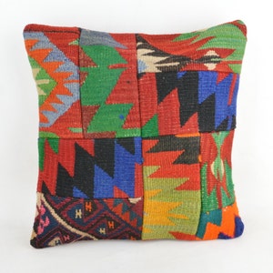Puede incluir: Cojín cuadrado de patchwork con una vibrante mezcla de colores. El diseño presenta patrones geométricos en rojo, verde, azul, naranja y negro. El cojín está hecho de una tela tejida, probablemente lana, y tiene un aspecto texturizado. El cojín mide aproximadamente 40 cm cuadrados.