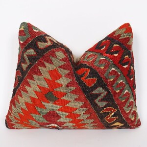 May include: A red, green, and black patterned throw pillow with a geometric design. The pillow is made of woven fabric and has a traditional look.