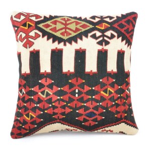 Puede incluir: Cojín decorativo cuadrado con un patrón geométrico en rojo, negro, crema y amarillo. El cojín presenta un diseño tejido con formas simétricas y un motivo central de diamante. El cojín probablemente está hecho de una tela duradera.