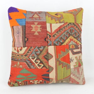 Könnte beinhalten: Quadratisches Patchwork-Kissen mit einer lebendigen Mischung aus Farben und geometrischen Mustern. Das Kissen weist eine Vielzahl von Texturen und Designs auf, darunter Rot, Orange, Grün und Beige. Das Kissen ist ein dekorativer Artikel.