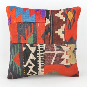 Könnte beinhalten: Quadratisches Patchwork-Kissen mit einer lebendigen Mischung aus Farben und Mustern. Das Kissen hat eine rote Basis mit verschiedenen geometrischen und abstrakten Designs in Blau, Schwarz, Weiß und Braun. Es ist ein dekoratives Wohnaccessoire.