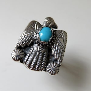 Op de afbeelding: Een zilveren ring met een turquoise steen in het midden, die een gestileerde adelaar met ingewikkelde details afbeeldt.