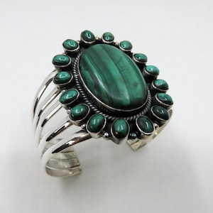 May include: A silver cuff bracelet featuring a large oval malachite stone surrounded by smaller malachite stones.
