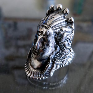 Peut inclure: Une bague en argent avec un design d&eacute;taill&eacute; d'une t&ecirc;te de personne portant une couronne. La bague est en m&eacute;tal et a une surface textur&eacute;e.