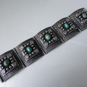 May include: A silver bracelet with five square turquoise stones set in a decorative design. The bracelet is made of linked sections that can be adjusted to fit different wrist sizes.
