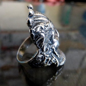 Peut inclure: Une bague en argent avec un design d&eacute;taill&eacute; et complexe d'un visage avec une couronne. La bague est en argent sterling et a une finition polie.
