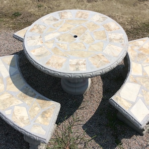 May include: A concrete patio set with a round table and two curved benches. The table and benches are decorated with a mosaic of light brown and beige stone tiles.
