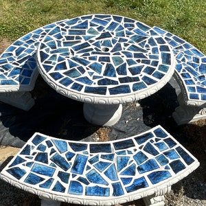 May include: A blue and white mosaic patio set with a round table and three curved benches. The table and benches are made of concrete and have a white base with a blue mosaic top.