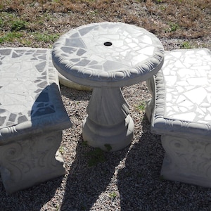 May include: A gray concrete patio set with a round table and two benches. The table and benches are decorated with a mosaic of gray and white tiles.
