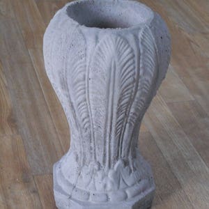 May include: A gray concrete planter with a decorative feather design. The planter has a wide, round opening and a hexagonal base.