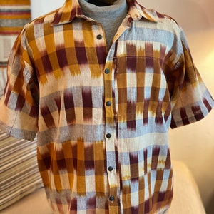 May include: A short-sleeved button-down shirt with a checkered pattern in shades of brown, white, and grey. The shirt has a relaxed fit and a classic collar.