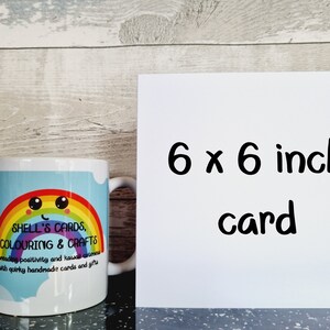 Peut inclure: Une tasse blanche avec un motif arc-en-ciel et le texte "SHELL'S CARDS, COLOURING & CRAFTS Spreading positivity and kawaii cuteness with quirky handmade cards and gifts". Une carte blanche avec le texte "6 x 6 inch card" est &agrave; c&ocirc;t&eacute; de la tasse.