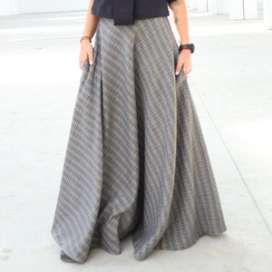 May include: A black short-sleeved top with a high neckline and a bow detail, paired with a long, flowing plaid skirt in shades of gray and tan. The skirt has a wide, A-line silhouette. The outfit is suitable for a variety of occasions.