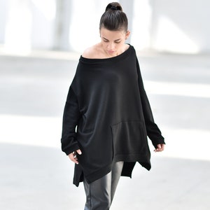 May include: A woman wearing a black oversized sweater with a large pocket and black leather pants. She is wearing black heeled boots.