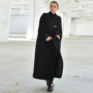 May include: A long black cape with a buckle closure. The cape is made of a soft, warm fabric and has a relaxed fit.