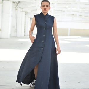 May include: A sleeveless, navy blue dress with a high collar and button-down front. The dress has a long, flowing skirt with a high slit, and is worn with sneakers. The dress is made of a textured fabric.