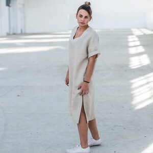 May include: A woman wearing a light beige linen dress with a side slit and white sneakers.