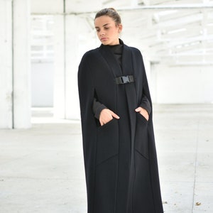 May include: A long black cape with a buckle closure and pockets. The cape is made of a thick, textured fabric.