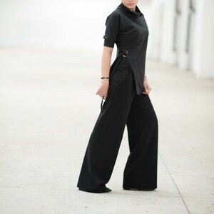 May include: A woman wearing a black mock neck top with a side tie detail and wide-leg black trousers.