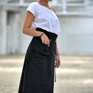May include: A black skirt with a large pocket on the front and a tie at the waist. The skirt is made of a soft, flowing fabric.