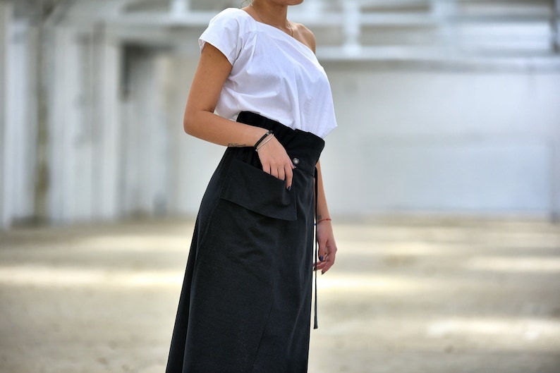May include: A black skirt with a large pocket on the front and a tie at the waist. The skirt is made of a soft, flowing fabric.