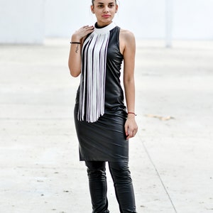 May include: A woman wearing a black leather dress with a white fringe collar and black leather boots.