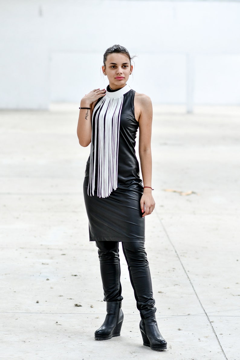May include: A woman wearing a black leather dress with a white fringe collar and black leather boots.