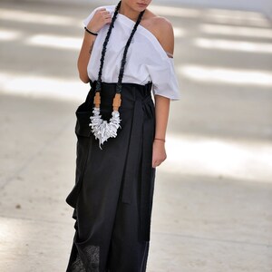 May include: A woman wearing a white off-the-shoulder top with a black and white necklace and a black wrap skirt.