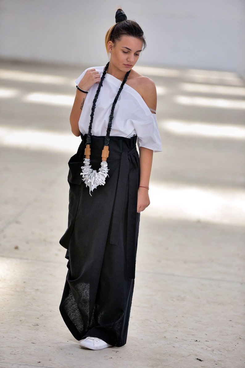 May include: A woman wearing a white off-the-shoulder top with a black and white necklace and a black wrap skirt.