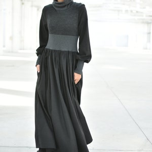 May include: A long black dress with a grey turtleneck top and long sleeves. The dress has a fitted bodice and a flowing skirt.