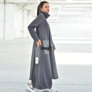 Puede incluir: Un vestido gris de manga larga con cuello alto y cintur&oacute;n negro. El vestido tiene un bolsillo de parche en el lado izquierdo y una etiqueta que dice "22/12".