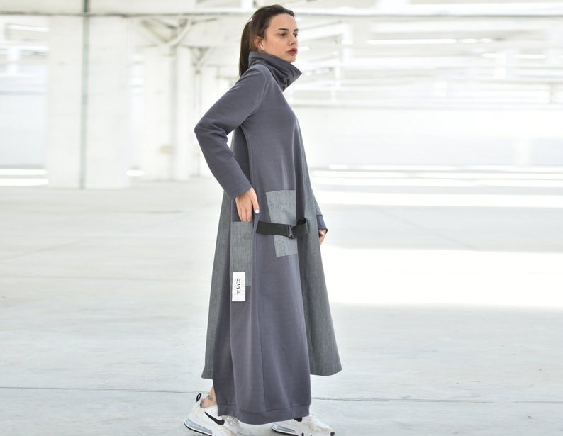 Puede incluir: Un vestido gris de manga larga con cuello alto y cintur&oacute;n negro. El vestido tiene un bolsillo de parche en el lado izquierdo y una etiqueta que dice "22/12".
