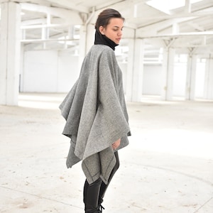 May include: A woman wearing a gray and white patterned poncho with black leggings and black lace-up boots.