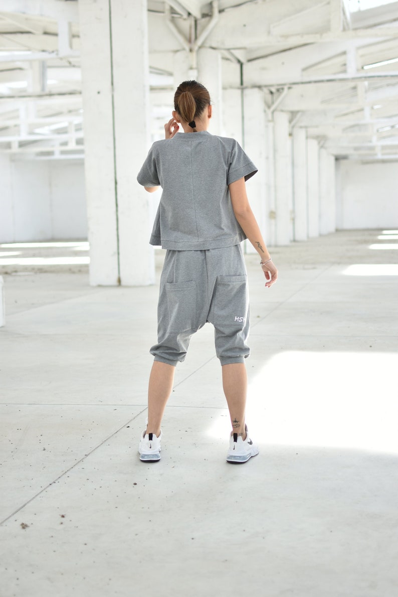 May include: A person wearing a gray, loose-fitting, short-sleeved top and matching gray sweatpants with a white logo. The person is wearing white sneakers.