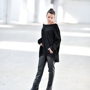 May include: A woman wearing a black off-the-shoulder sweater and black leather pants with a wedge heel boot.