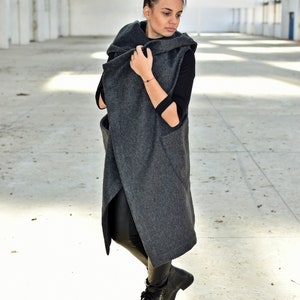 May include: A long, gray, hooded cardigan with a wrap-around style. The cardigan is worn over a black long-sleeved shirt and black pants. The person is wearing black boots.