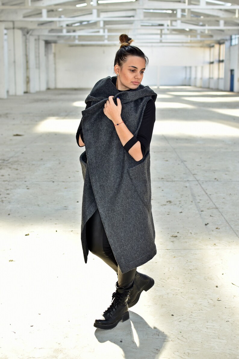 May include: A long, gray, hooded cardigan with a wrap-around style. The cardigan is worn over a black long-sleeved shirt and black pants. The person is wearing black boots.