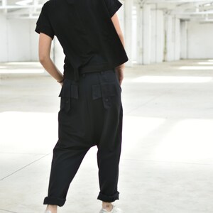 May include: A person wearing a black short-sleeved shirt and black pants with large pockets. The person is wearing white sneakers.
