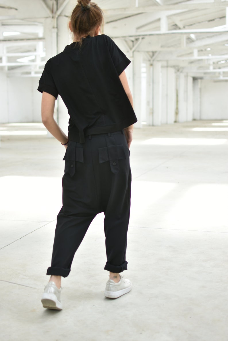 May include: A person wearing a black short-sleeved shirt and black pants with large pockets. The person is wearing white sneakers.