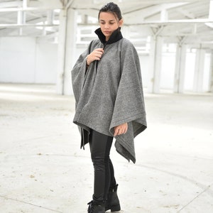 May include: A woman wearing a gray and black houndstooth poncho with a black turtleneck underneath. She is wearing black leggings and black combat boots.